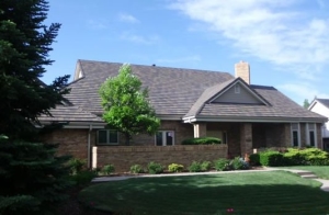 A tan brick house with a green lawn and green shrubs and trees.