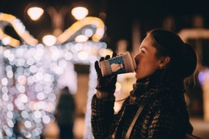 a woman drinking from a snowman cup outside at night with holiday lights in the background