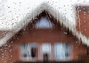 Rain dripping down a glass window with a blurry house in the background